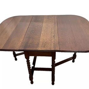 May include: A dark brown wooden drop leaf table with a rounded oval top and a carved, twisted base. The table has a simple design and is in good condition.