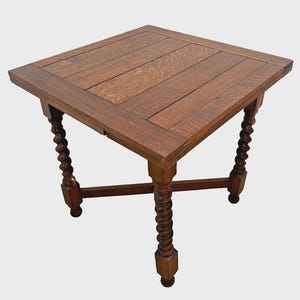 May include: A square wooden table with a medium brown finish and a planked top surface. The table features four legs with a distinct spiral-turned design, connected by a cross-shaped stretcher base that provides structural support.