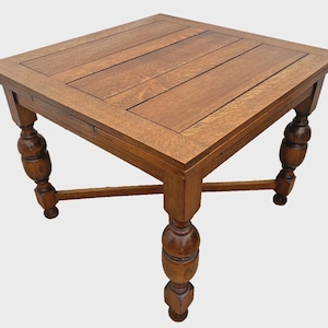 May include: A square wooden table with a medium brown finish and a planked top surface. The table features four legs with a turned, bulbous design and a cross-stretcher base connecting the legs for stability. The wood grain is visible throughout.