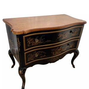 May include: A black painted chest of drawers with gold accents and floral designs. The chest has two drawers and sits on four cabriole legs. The top of the chest is made of wood.