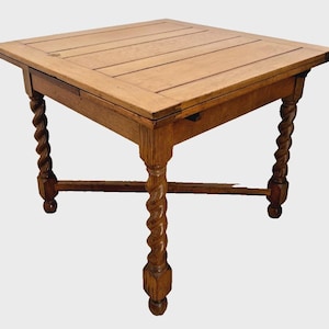 May include: A square wooden table featuring a light brown finish and a planked top surface. The table is supported by four legs with a distinct spiral twist design, connected by a lower cross-stretcher frame that provides structural stability.