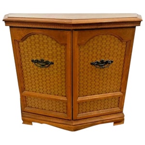 May include: A wooden cabinet with two doors and a woven pattern. The cabinet has a curved front and black metal handles.