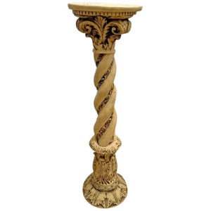 May include: A tall, cream-colored pedestal with a twisted column and intricate carvings. The pedestal has a round top and a base with a decorative design.