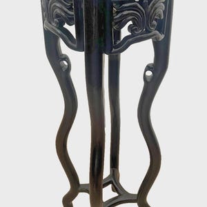 May include: A dark blue, glossy pedestal stand featuring a circular top surface and four curved, slender legs. The upper section of the stand is decorated with intricate, carved scrollwork patterns that connect the legs to the tabletop.