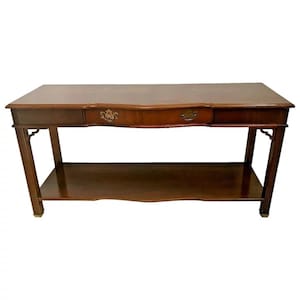 May include: A dark brown wooden console table with a curved top and a single drawer. The table has a lower shelf and decorative legs.