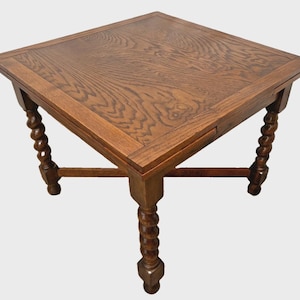 May include: A square wooden table with a medium brown finish and a visible wood grain pattern on the top surface. The table features four legs with a distinct spiral twist design, connected by a cross-shaped stretcher base underneath.