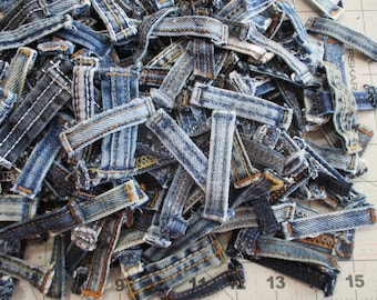 Könnte beinhalten: Eine große Ansammlung von blauen Jeans-Gürtelschlaufen in verschiedenen Indigo-Tönen, von hell bis dunkel gewaschen. Jede einzelne Schlaufe weist verstärkte Nähte in goldfarbenem, weißem oder blauem Garn auf und zeigt ausgefranste Kanten.