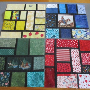 May include: Four fabric squares with a patchwork design. Each square is made up of smaller squares of different colors and patterns, including red, white, blue, green, yellow, and black. The squares are arranged in a grid pattern.