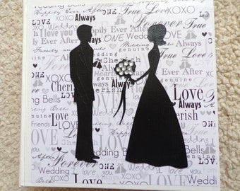 May include: A white scrapbook with a black silhouette of a bride and groom. The background is covered in a white and gray pattern with the words "Love", "Wedding", "Forever", "True", "Always", and "Cherish" repeated throughout.