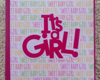 May include: Pink and white scrapbook with the words "It's a Girl!" in large pink letters. The background is a repeating pattern of the words "Sweet Baby Girl".