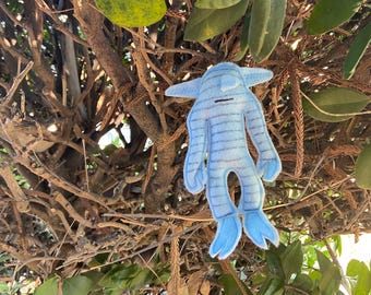 May include: A blue felt toy with a striped pattern and a black face. The toy is hanging from a branch in a tree.