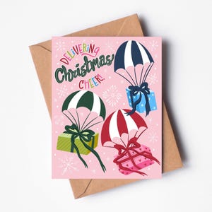 Tarjeta "Entregando alegría navideña": adorable tarjeta navideña con regalos y paracaídas, divertida tarjeta de felicitación navideña rosa, tarjeta festiva única