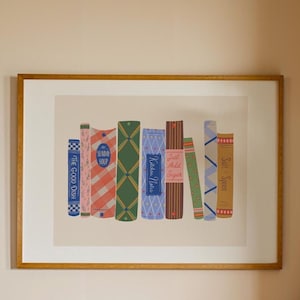 May include: A framed print featuring stylized illustrations of cookbooks. The books have various patterns and colors, including plaid, floral, and geometric designs. Text on the spines reads "The Good Dish," "Sunday Soup," "Kitchen Notes," and "Just Add Sugar."