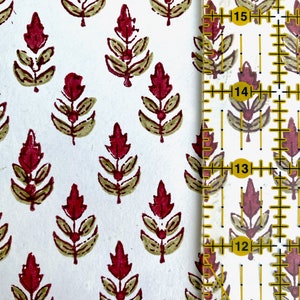A close up view of cotton rag paper hand block printed with an Indian Buti floral design in scarlet red. The paper color is ivory and the image shows a ruler next to the flowers to indicate print scale.