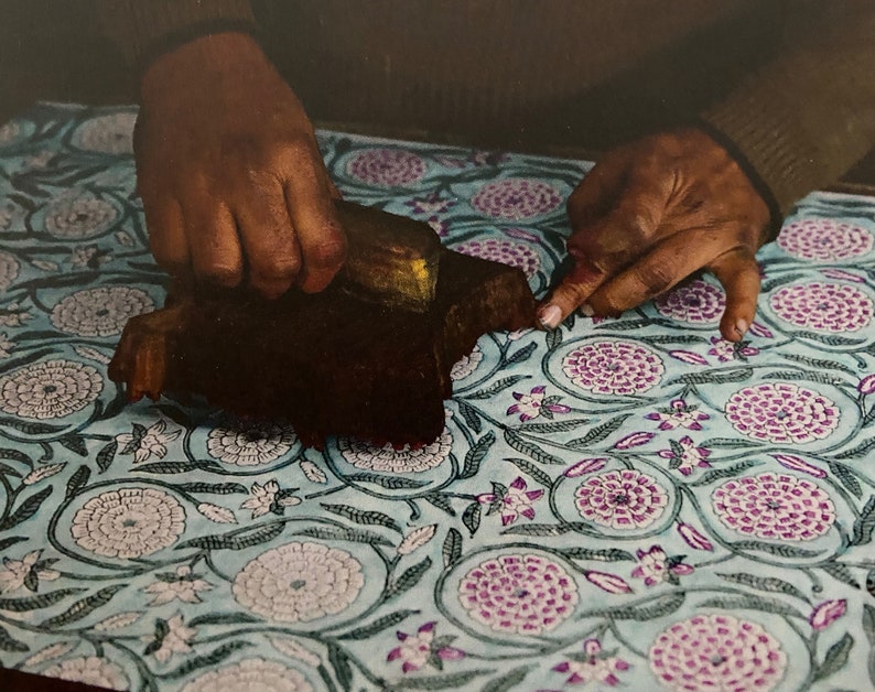 An artisan printing a floral design on cotton rag paper using a traditional wooden block to apply the ink.