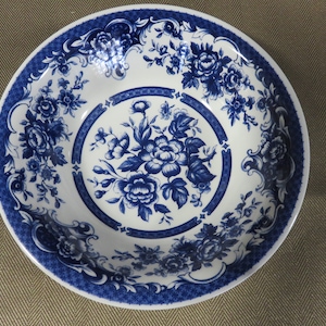 May include: A white ceramic bowl with a blue and white floral pattern. The bowl has a wide rim and a deep well.