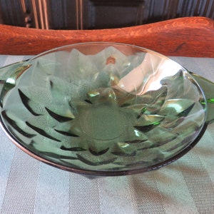 May include: A green glass bowl with a scalloped edge and two handles. The bowl has a textured, floral design.