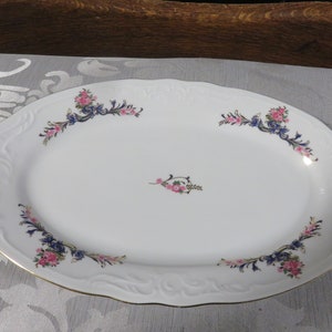May include: White oval serving platter with a gold rim and floral design. The flowers are pink and blue with green leaves.
