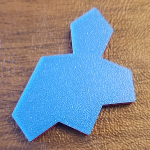 May include: A blue, geometric-shaped object with a textured surface and red edges. The object is placed on a brown, textured surface. The shape has a unique design.
