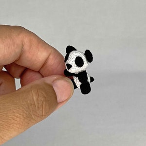 May include: A small crocheted panda bear toy with black and white fur. The panda is sitting up with its arms crossed.