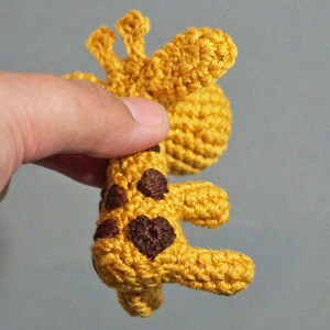 May include: A crocheted giraffe toy with brown spots and a yellow body. The giraffe is standing on its hind legs with its front legs outstretched.