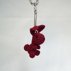 May include: A red crocheted bunny keychain with black eyes. The bunny is attached to a silver chain.