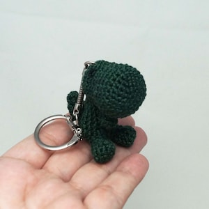 May include: A green crocheted dinosaur keychain with a silver metal ring.