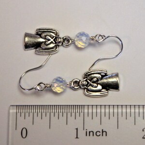 May include: Silver angel earrings with white opal beads. The earrings are approximately 1 inch long.