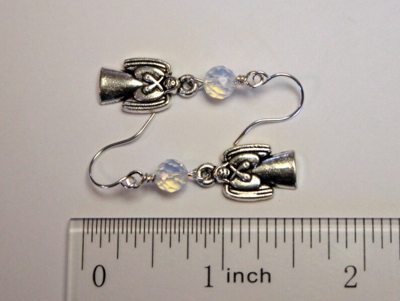 May include: Silver angel earrings with white opal beads. The earrings are approximately 1 inch long.