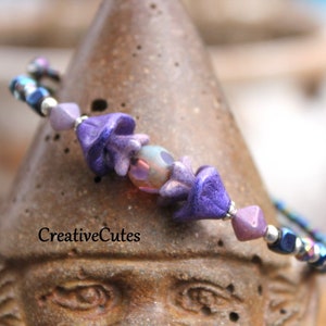 May include: Purple and silver beaded bracelet with a flower charm. The bracelet is on a brown surface.