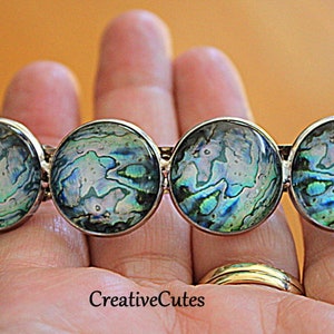 May include: Four round silver hair clips with iridescent abalone shell inlays. The shell has a blue, green, and white pattern.