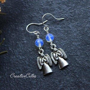 May include: Silver angel earrings with blue opal beads. The angels are facing forward with their wings outstretched. The earrings are hanging from silver hooks.