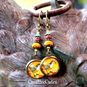 May include: A pair of dangle earrings with a bird design on the bottom. The earrings are made with gold-toned metal and feature a mix of yellow, red, and turquoise beads.