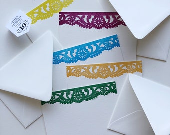 May include: A set of white stationery with colorful floral cut-out borders in yellow, purple, blue, gold, and green. The stationery is accompanied by white envelopes and a small tag with text.