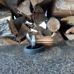May include: A silver and wood coffee tamper with a red stripe, sitting on a black rubber base.