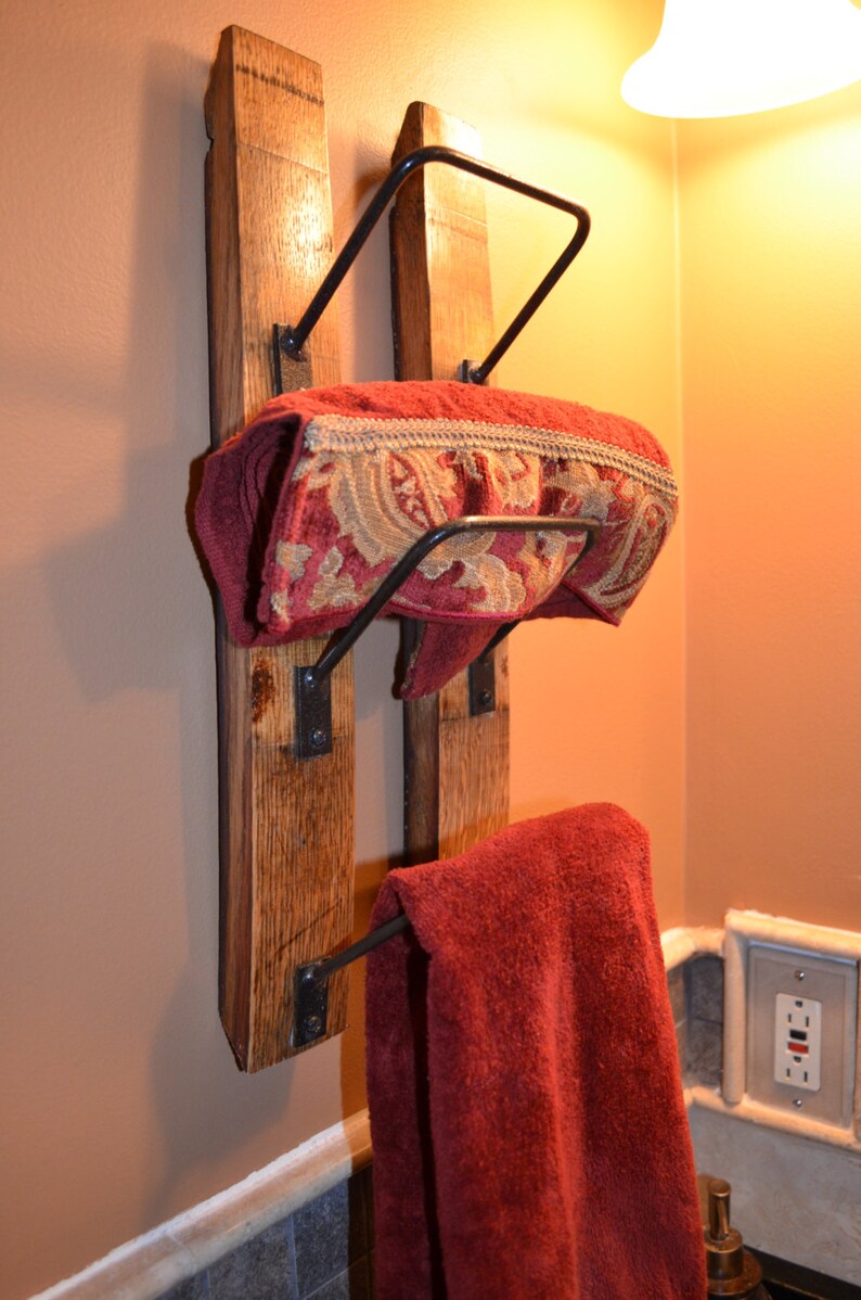 K&ouml;nnte beinhalten: Rustikaler Handtuchhalter aus Holz mit zwei Ebenen. Der Halter hat einen dunklen Metallrahmen und h&auml;lt zwei rote Handt&uuml;cher, eines gefaltet und das andere h&auml;ngend. Das gefaltete Handtuch hat eine dekorative Bord&uuml;re.