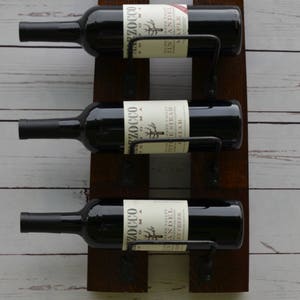 May include: A rustic wooden wine rack with three bottles of red wine. The rack is made of reclaimed wood and has a dark brown finish. The bottles are labeled with the names of the wines, including "ZIn ANDEL", "PETITE SIRAH", and "ANDEL BY CREEK".