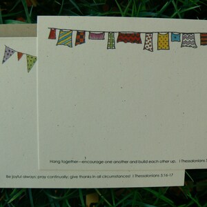 Op de afbeelding: Cr&egrave;mekleurige briefpapier set met een handgetekende illustratie van kleurrijke vlaggen en waslijnen. De set bevat notecards, enveloppen en een banner met hangende kledingstukken. De tekst luidt: "Hang together..." en "Be joyful always..."