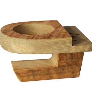 May include: A handcrafted wooden cup holder with a natural finish. The holder features a circular indentation for a cup and a rectangular base. The wood grain is visible, adding to its rustic charm. The holder is designed to be mounted on a surface.