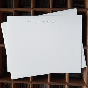 Puede incluir: Dos tarjetas de papeler&iacute;a blancas en blanco con el nombre "Danielle Chargo" en relieve en el centro superior de la tarjeta.
