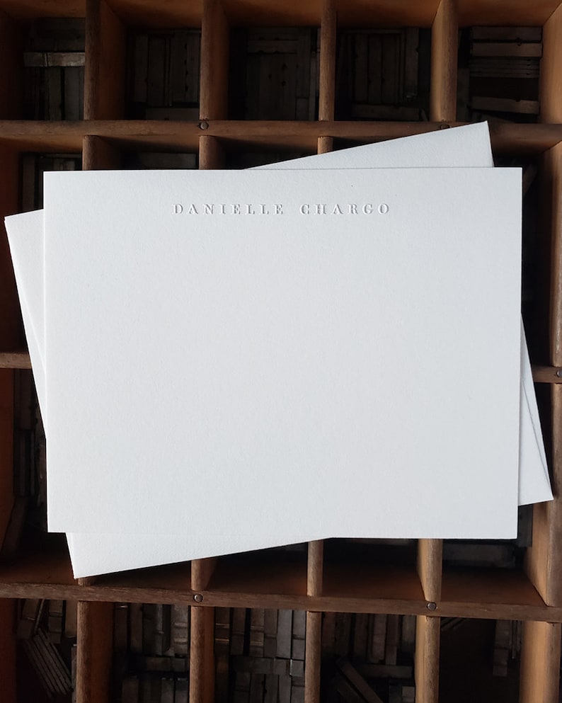 Puede incluir: Dos tarjetas de papeler&iacute;a blancas en blanco con el nombre "Danielle Chargo" en relieve en el centro superior de la tarjeta.