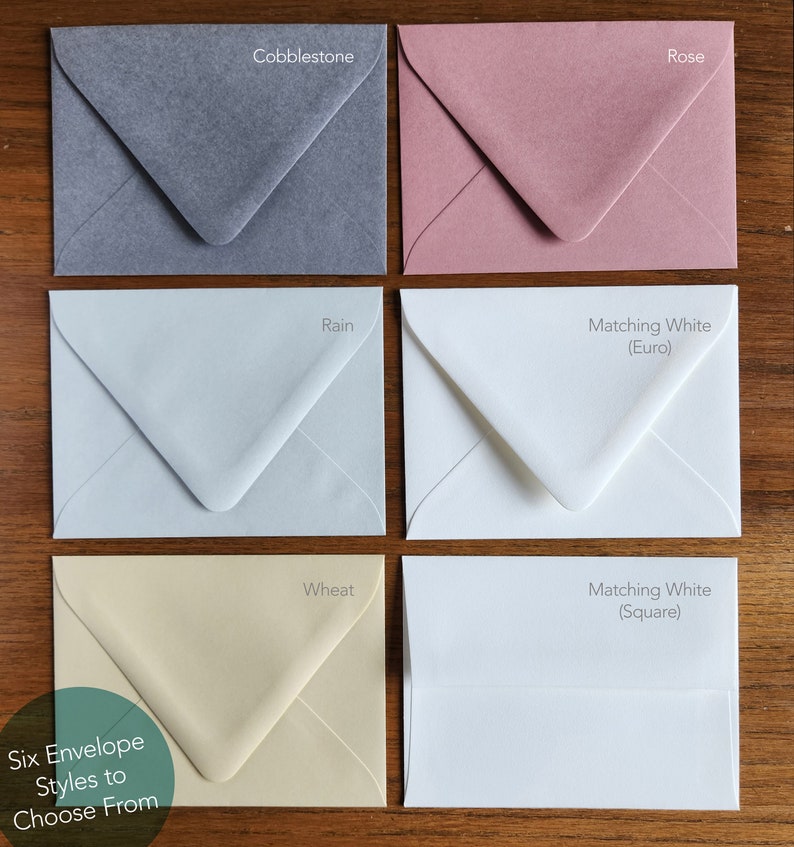 Puede incluir: Seis estilos diferentes de sobres mostrados en una superficie de madera. Los colores son Cobblestone (gris), Rain (azul claro), Rose (rosa), Wheat (crema), Matching White (Euro) y Matching White (Square).