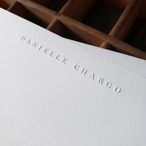 Puede incluir: Una tarjeta blanca con el nombre "Danielle Chargo" en relieve en una fuente simple y elegante.