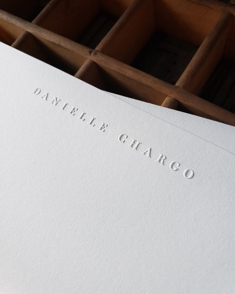 Puede incluir: Una tarjeta blanca con el nombre "Danielle Chargo" en relieve en una fuente simple y elegante.