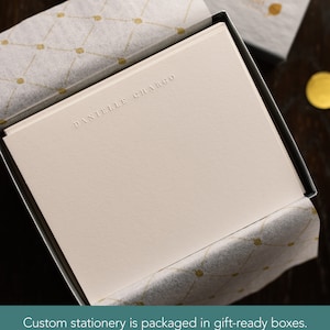 Puede incluir: Una caja blanca con una tarjeta blanca en su interior. La tarjeta tiene el nombre "DANIELLE CHARGO" en relieve en letras doradas. La caja est&aacute; forrada con papel de seda blanco con un patr&oacute;n dorado.