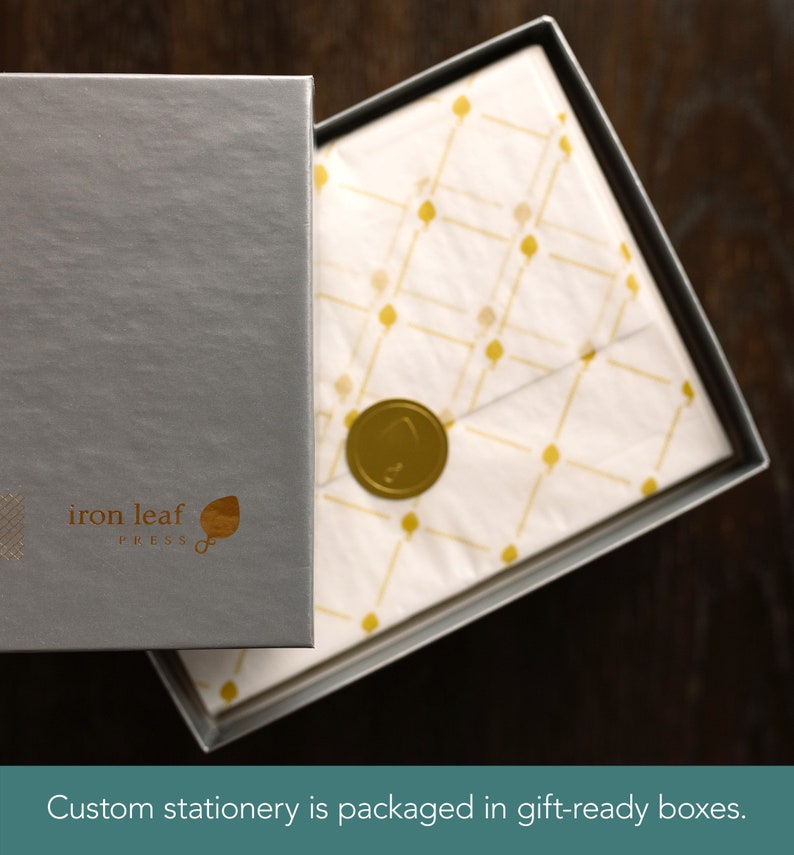 Puede incluir: Una caja plateada con el texto "iron leaf press" y un logotipo de hoja. La caja est&aacute; abierta, revelando papel de seda blanco con un patr&oacute;n dorado y un sello de cera dorado.