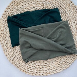May include: Two fabric headbands, one dark green and one olive green, are folded and displayed on a woven straw surface.