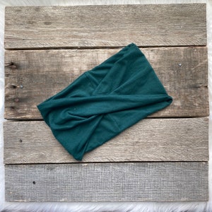 May include: A dark green fabric headband with a twisted knot design. The headband is made of a soft, stretchy material.