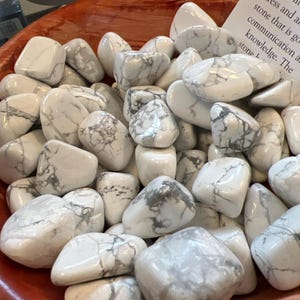 May include: A bowl filled with white howlite tumbled stones. The stones have a white and gray marbled pattern.