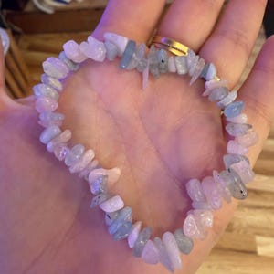 May include: A stretch bracelet composed of irregular, tumbled chip-style gemstones in alternating shades of pale pink and light blue. The stones are strung together on an elastic cord, creating a flexible circular band of polished mineral fragments.